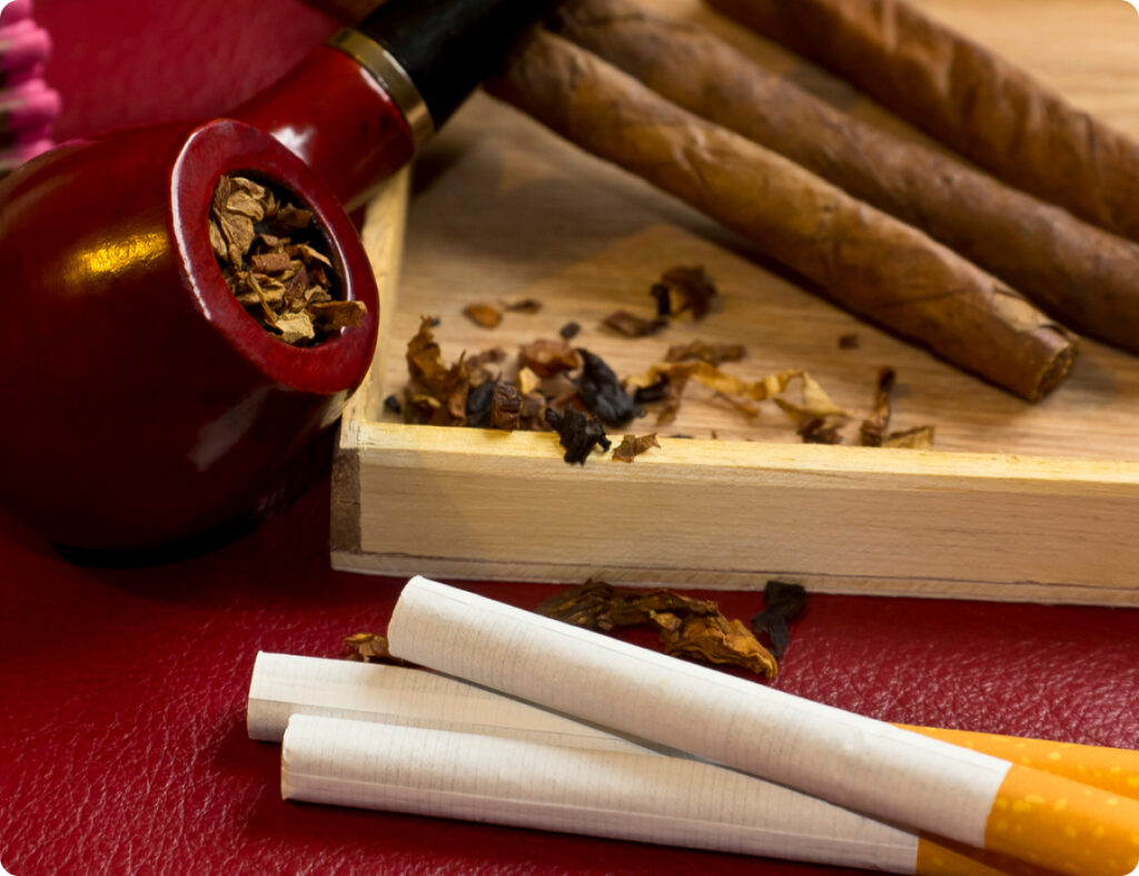 pipa piena di tabacco appoggiata su un vassoio di legno assieme a delle sigarette dei sigari