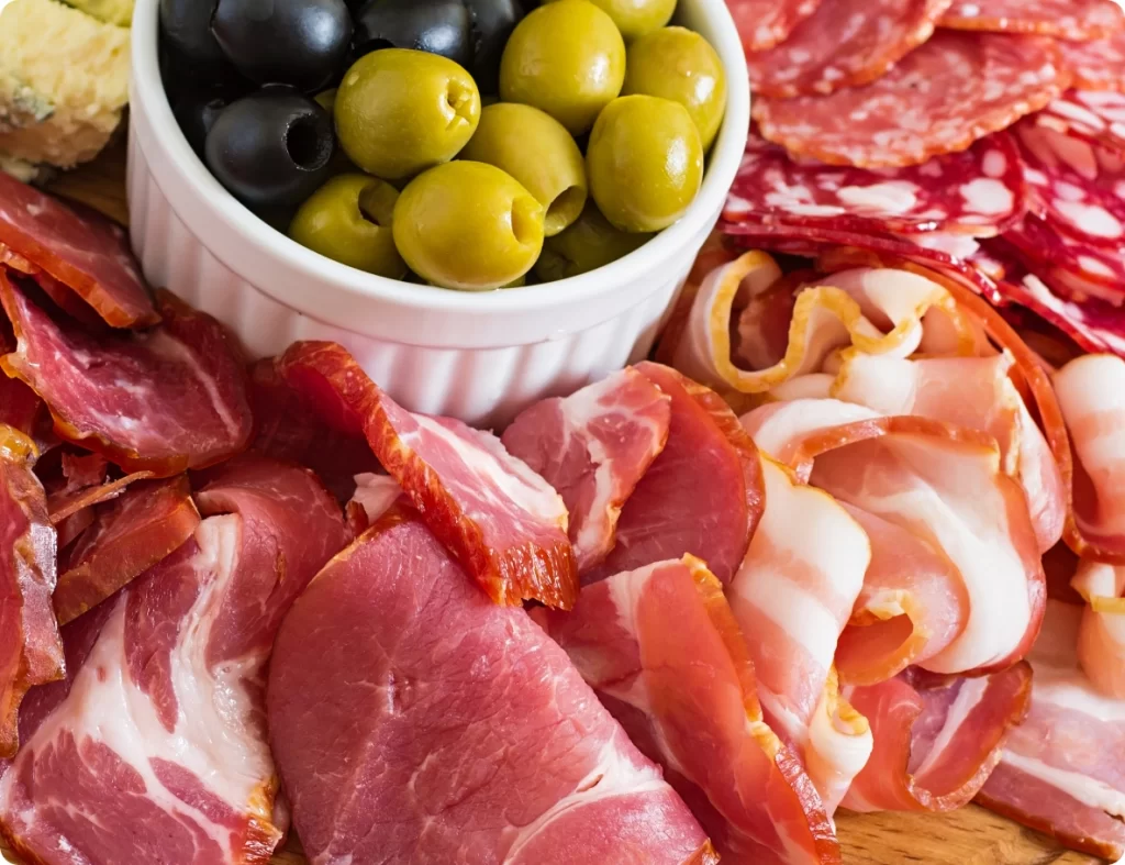 Primo piano di salumi di diverse tipologie con una ciotola di olive